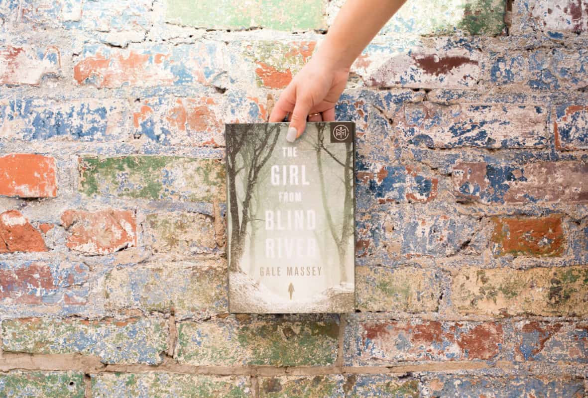 The Girl From Blind River held in front of a multicolored brick wall