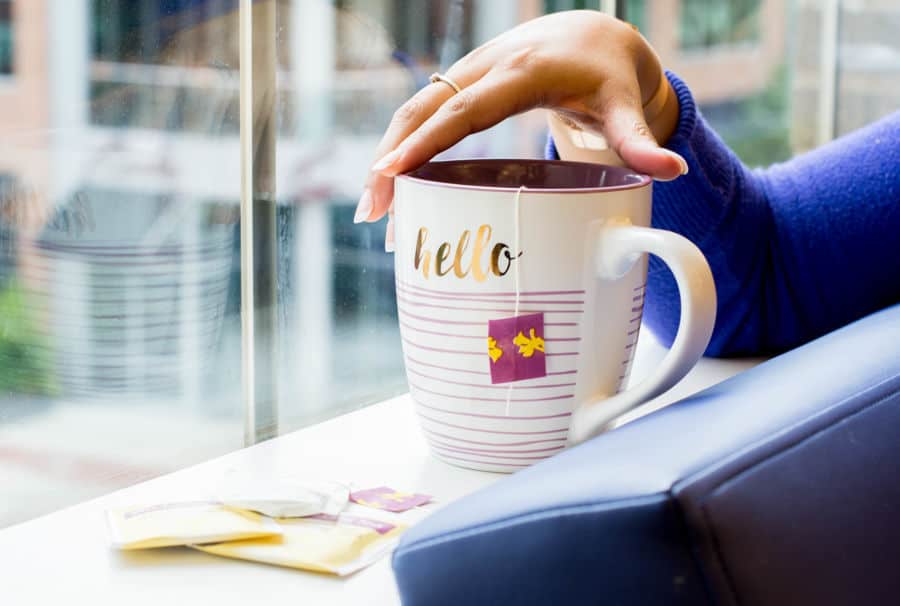 Woman looking out a window drinking tea in a mug that says hello