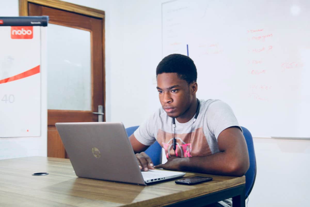 A view of a young man working behind a laptop.