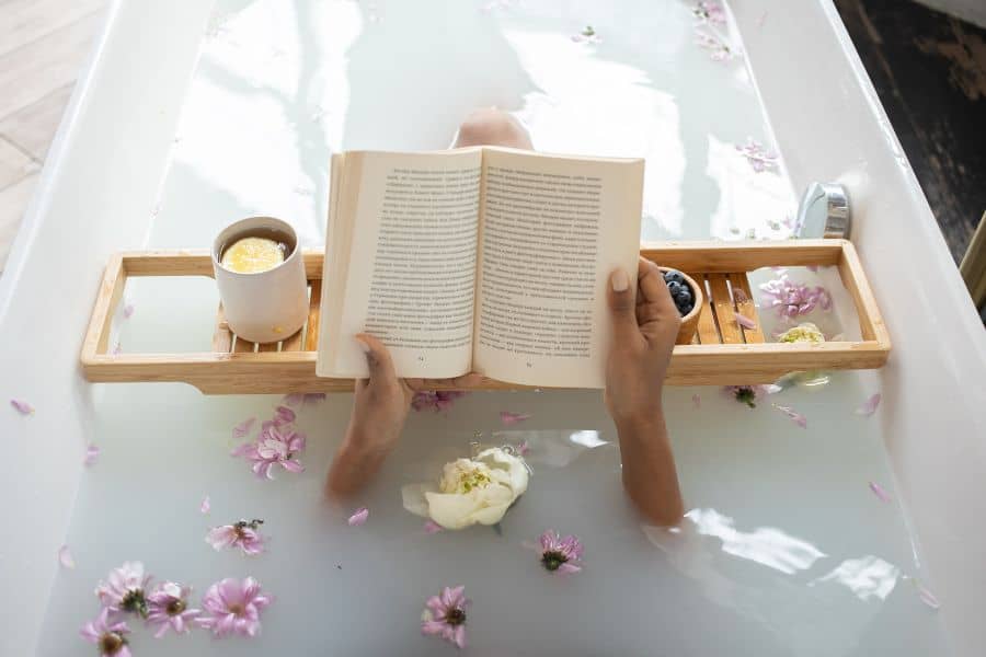 Person taking a relaxing bath and reading a book for self care