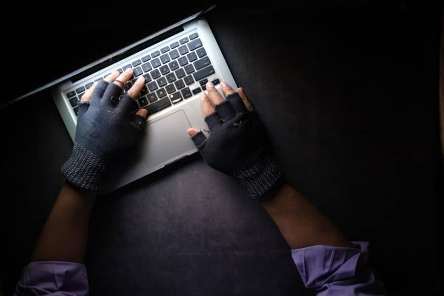 Dark image with hands of a hacker typing on a laptop keyboard