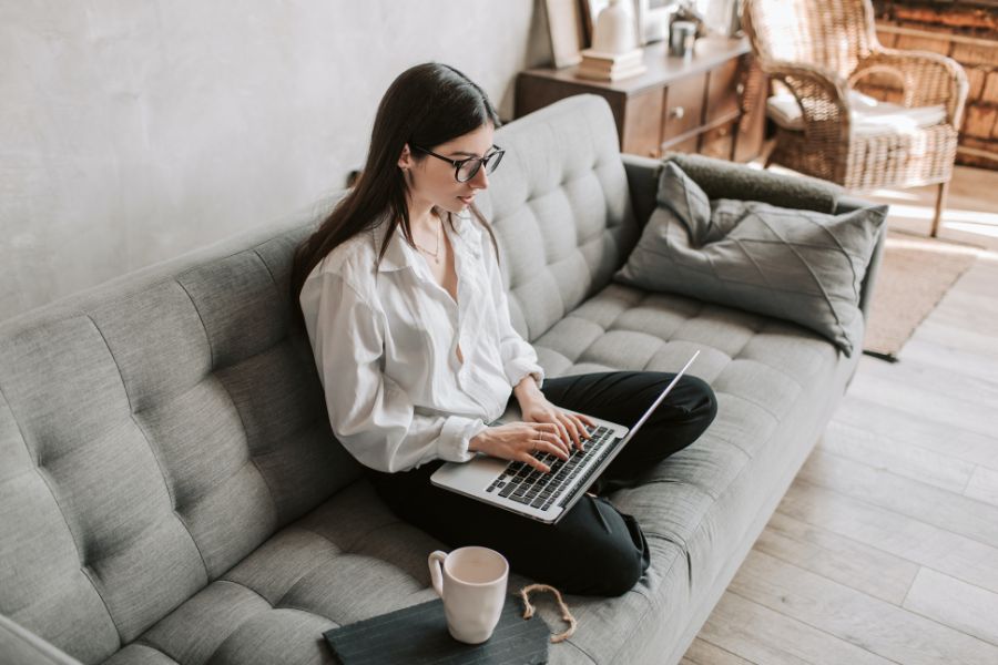 Woman sitting on couch using a laptop to hustle